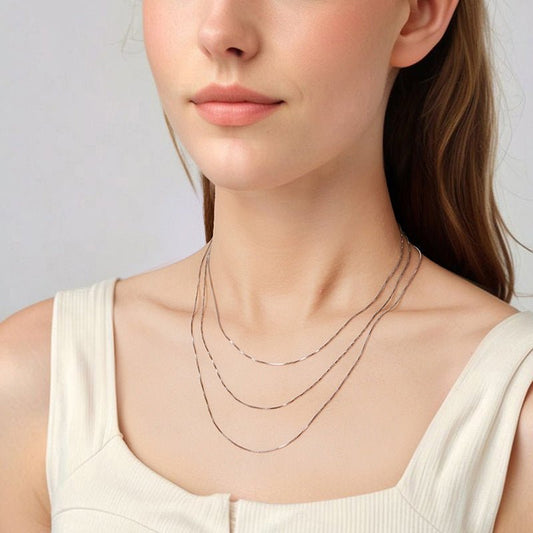 Woman wearing a delicate box necklace chain against a plain background.