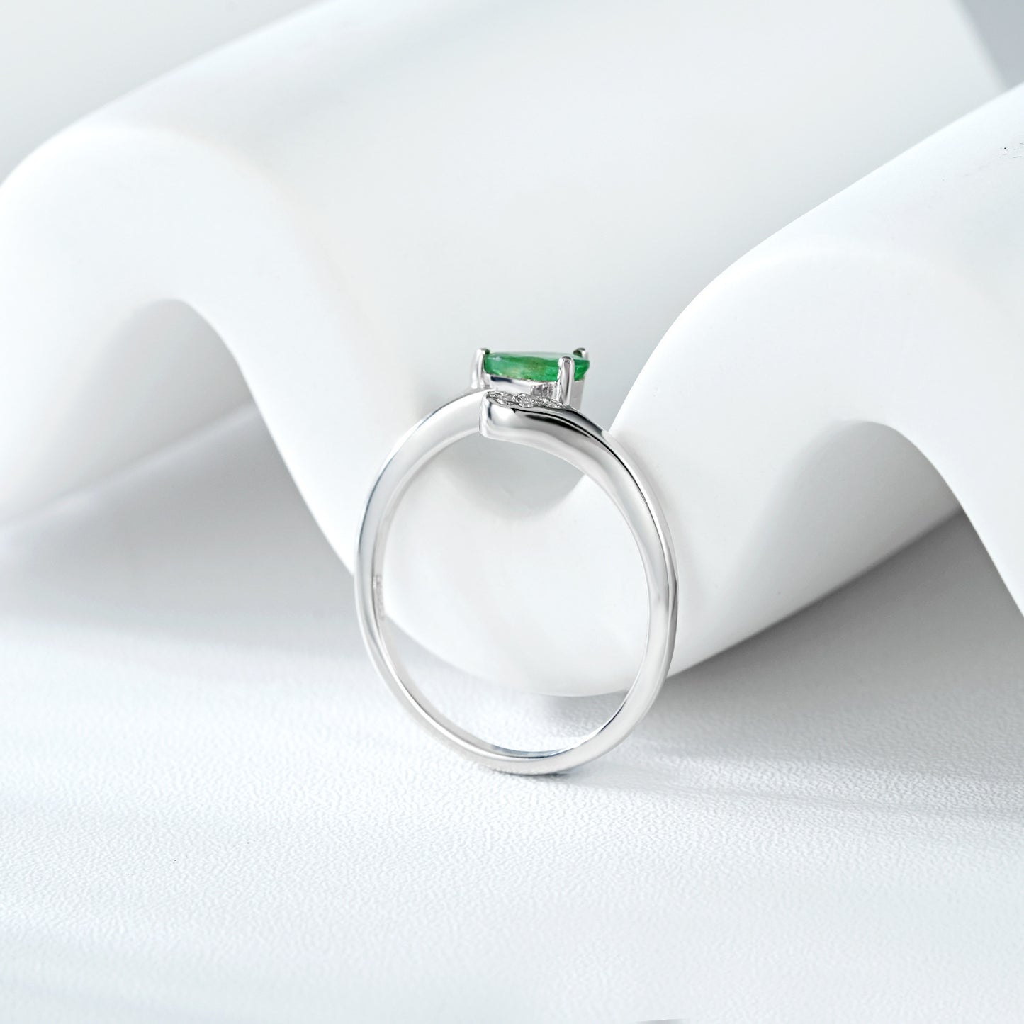 Silver ring with a green emerald gemstone on a white fabric background