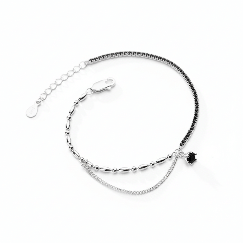 Silver bracelet with a small black heart charm and black stones in one side on a white background