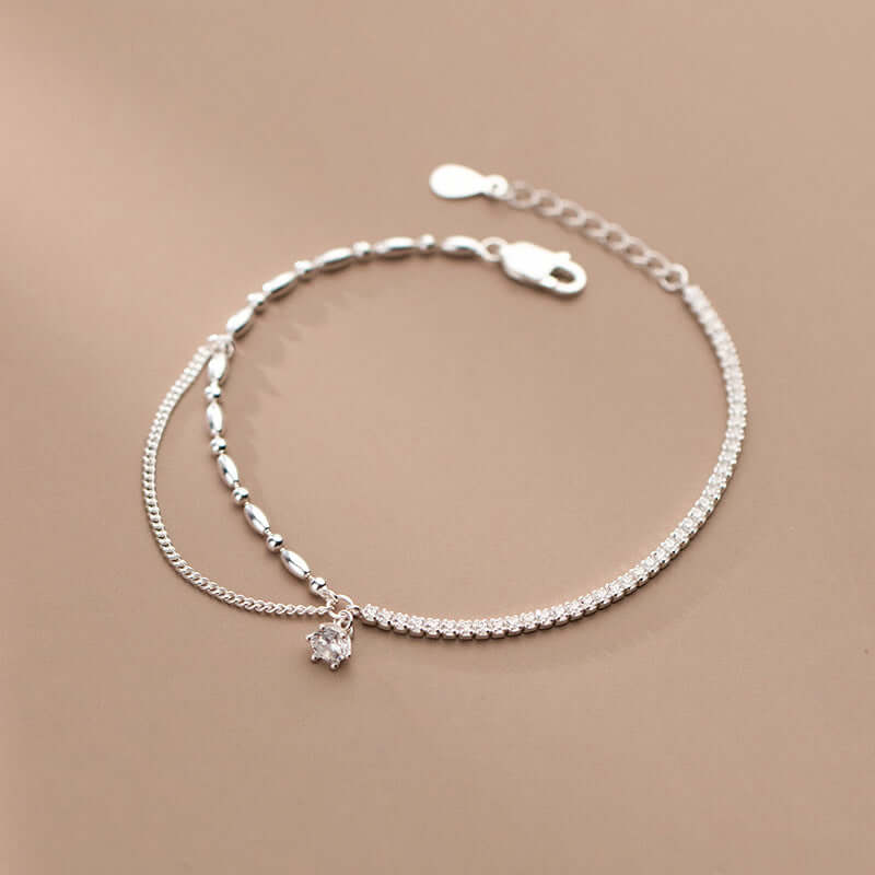 Silver anklet with a small crystal charm on a beige background