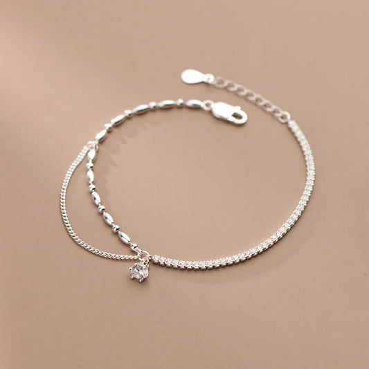 Silver anklet with a small crystal charm on a beige background