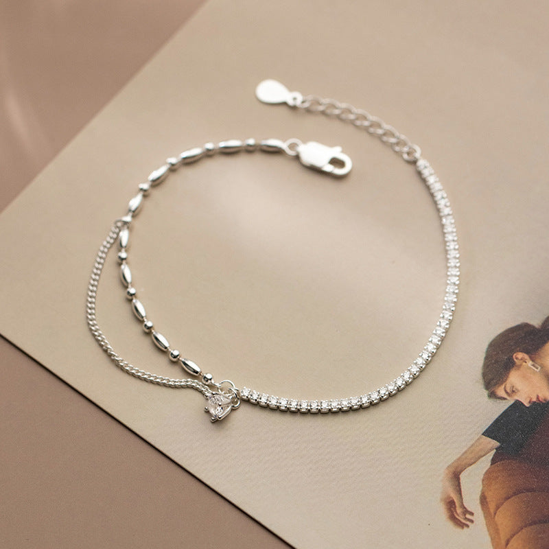 Silver bracelet with a white heart charm and white stones in one side on a beige surface