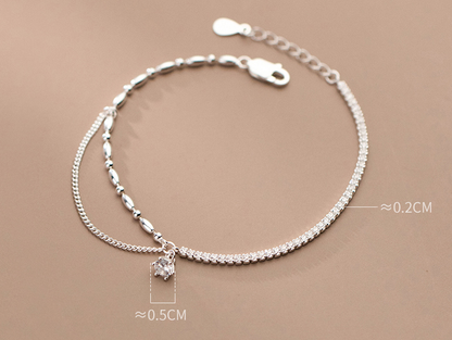 Silver anklet with a small white charm on a beige background with stone sizes specifications