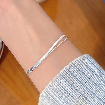 Silver Double Layer Snake Chain bracelet on a person's wrist with a blurred wooden background