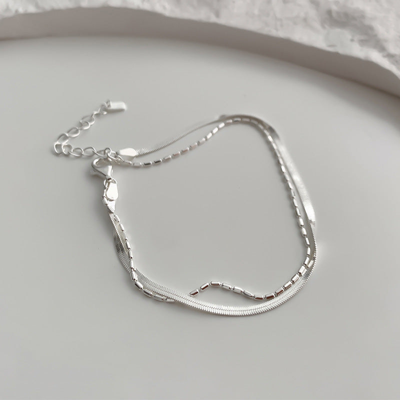 Silver double layer snake chain bracelet on a light gray surface