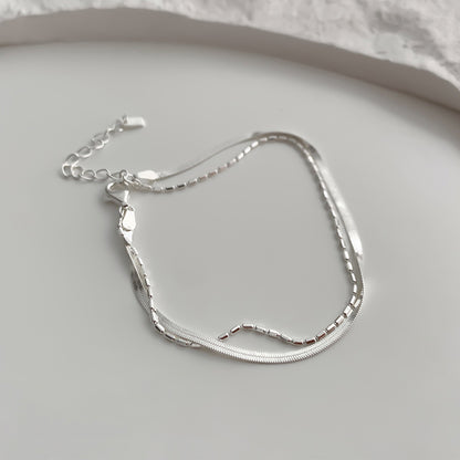 Silver double layer snake chain bracelet on a light gray surface