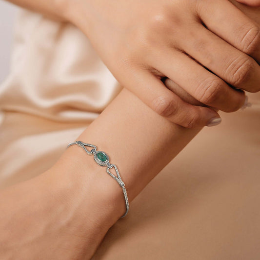 Silver bracelet with a main green emerald gemstone and white zirconia stones on a wrist against a beige background