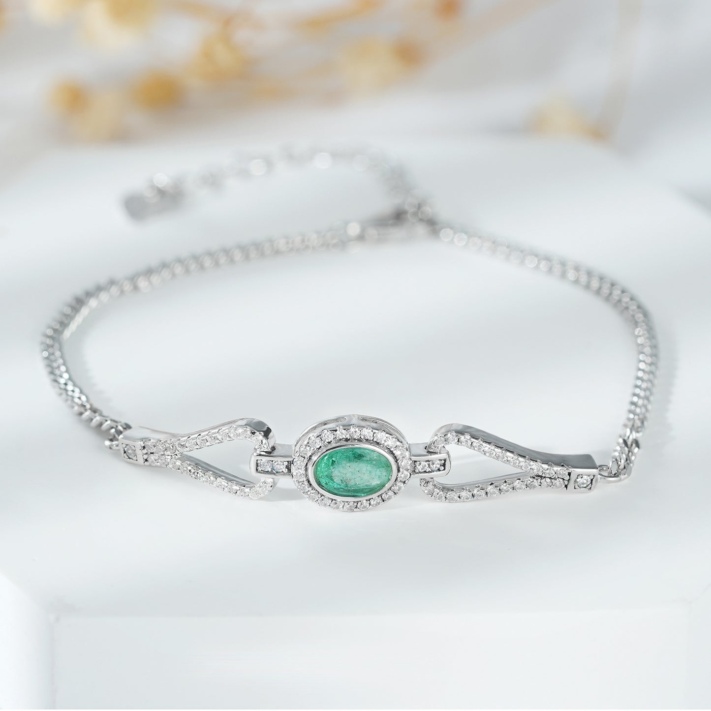 Silver bracelet with a main green emerald gemstone and white zirconia stones on a white background