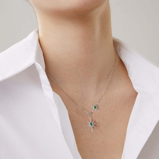 Necklace with two star shaped pendants and green emerald gemstones worn by a person in a white shirt