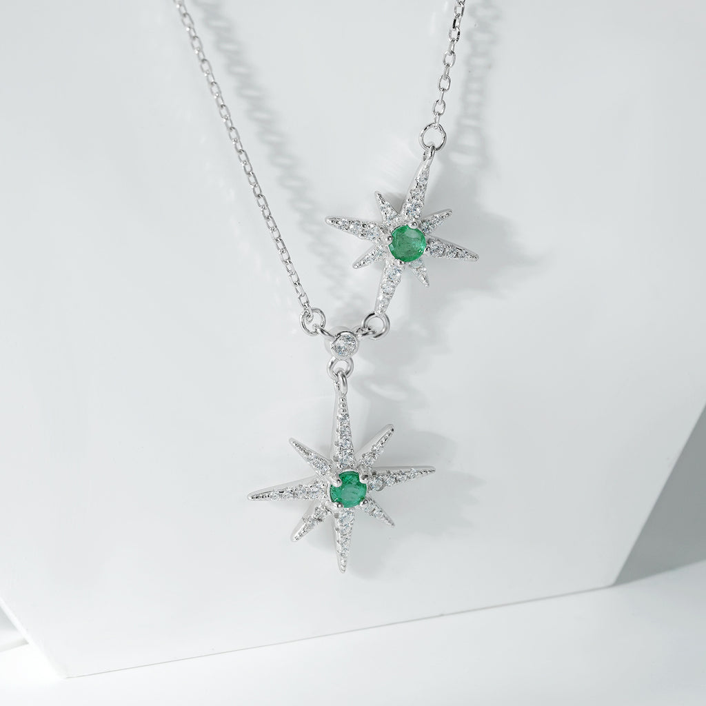 Silver necklace with star-shaped pendants and green emerald gemstones on a white background