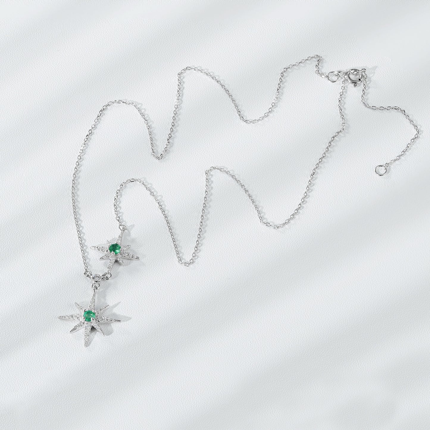 Silver necklace with star-shaped pendants on a light gray background
