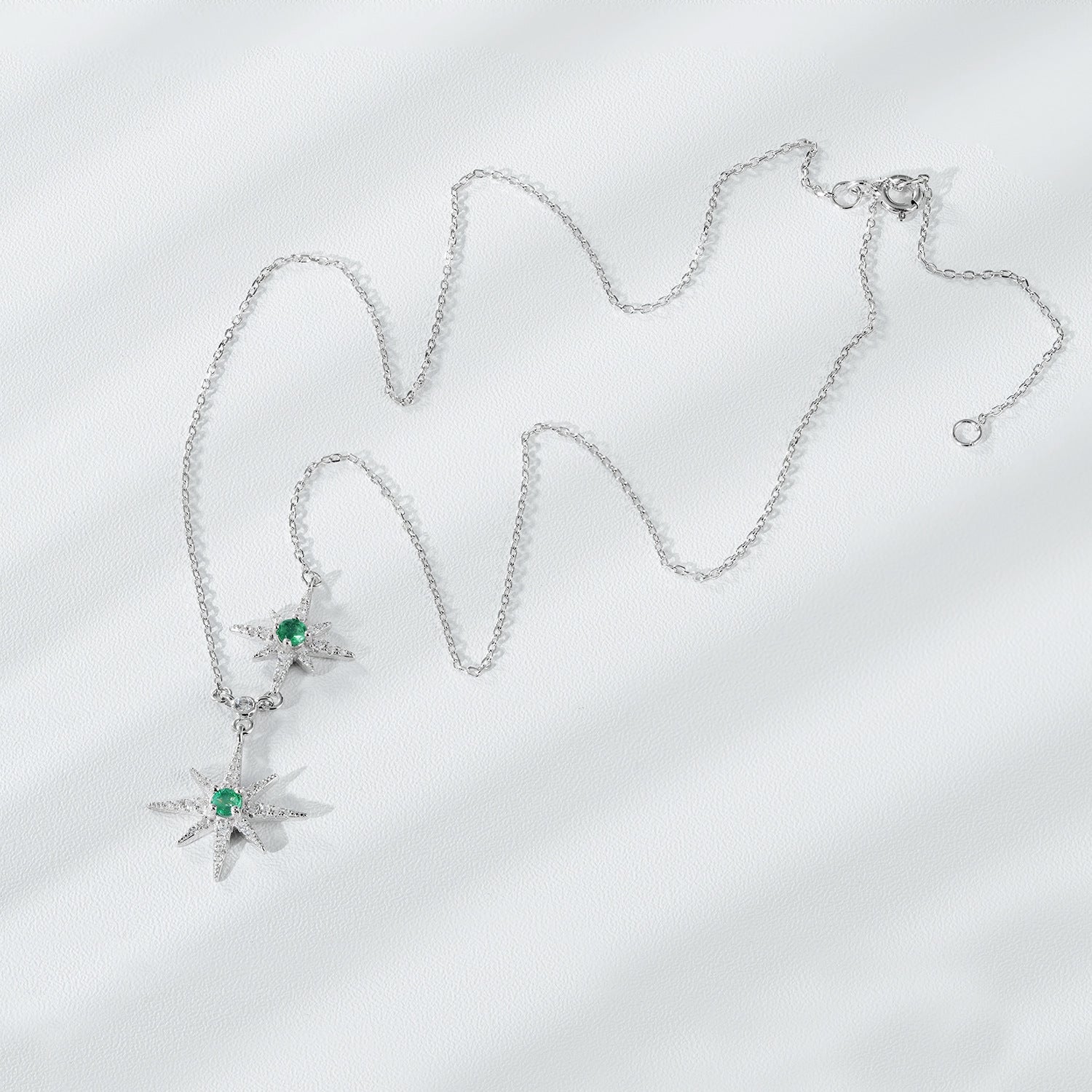 Silver necklace with star-shaped pendants on a light gray background