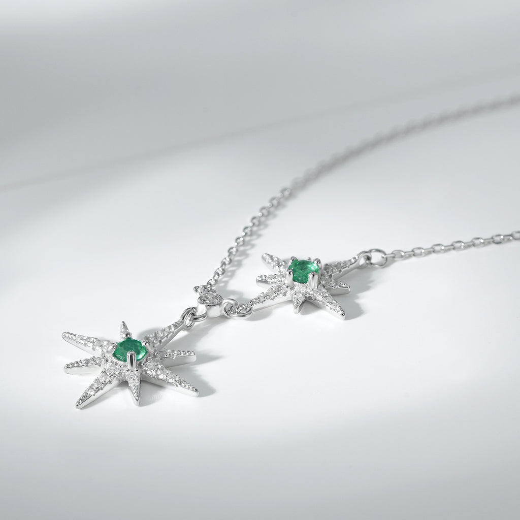 Silver necklace with star pendants and green emerald gemstones on a light gray background
