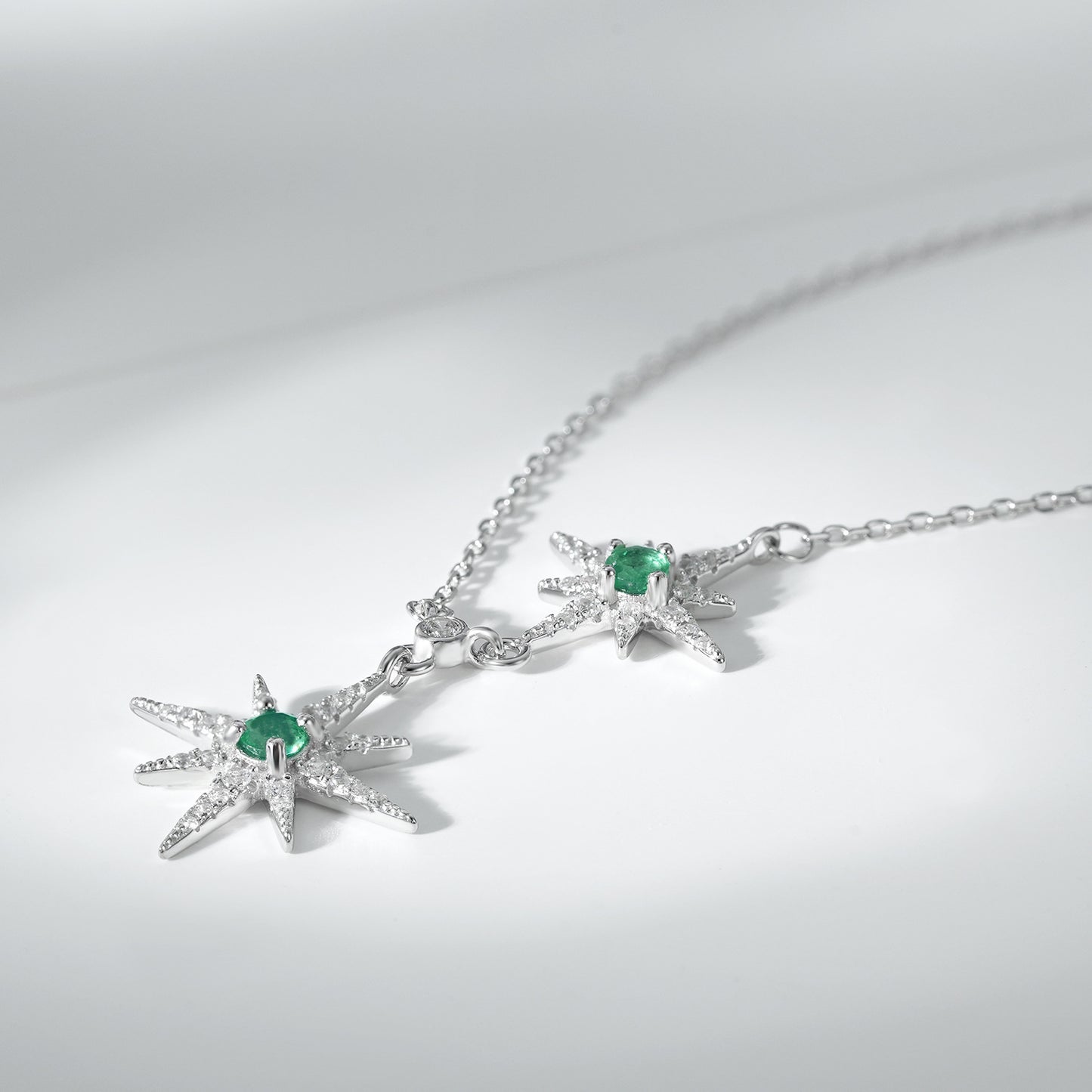 Silver necklace with star pendants and green emerald gemstones on a light gray background