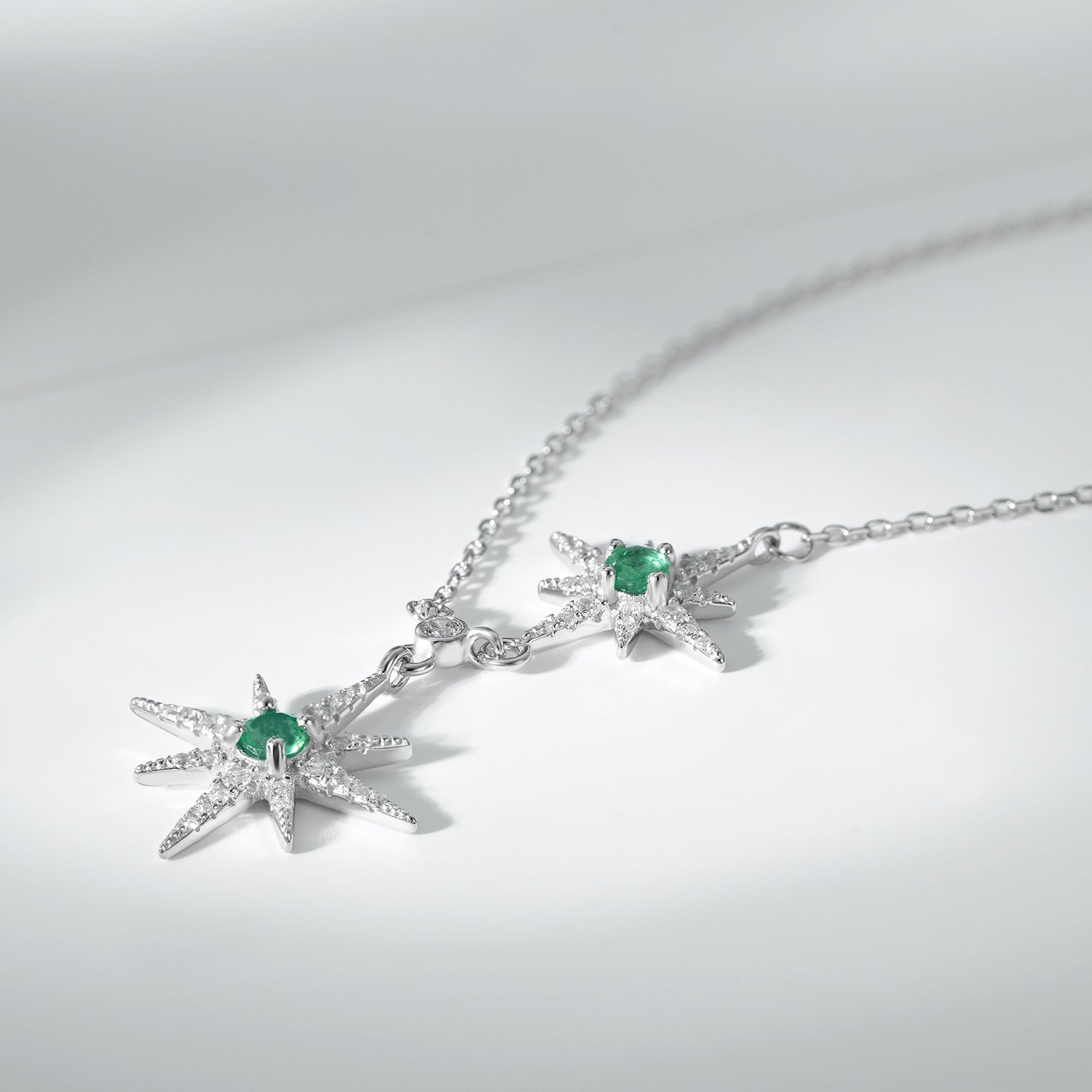 Silver necklace with star pendants and green emerald gemstones on a light gray background