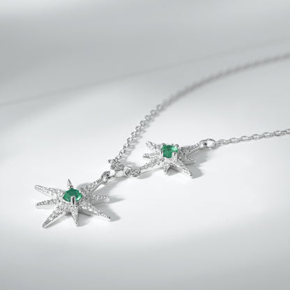 Silver necklace with star pendants and green emerald gemstones on a light gray background
