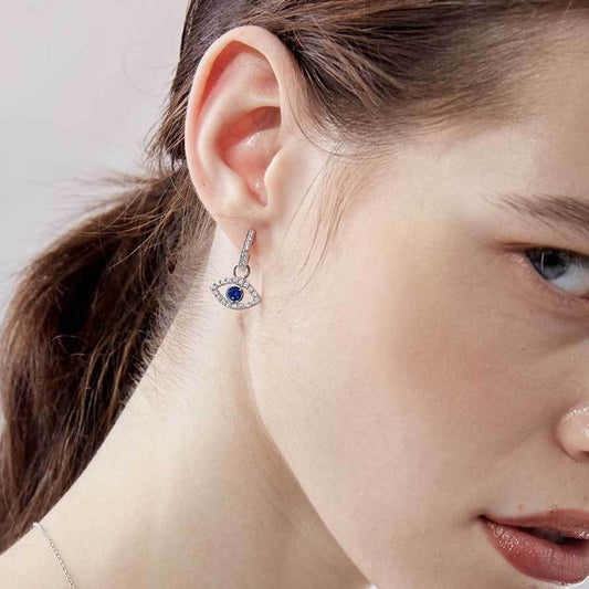 Close-up of a woman wearing eveil eye drop earring with a blue and white gemstone.