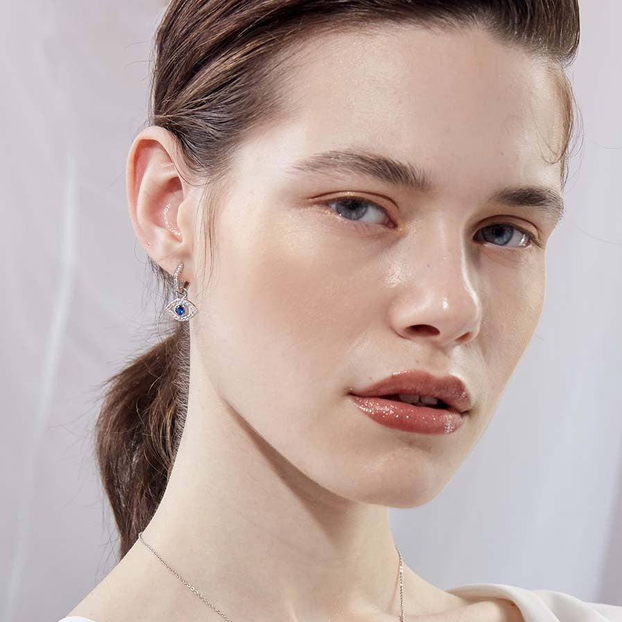 Close-up of a woman wearing an earring with a blue and white gemstones on a plain background