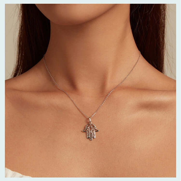 Silver Fatima hand necklace on a person's neck against a neutral background
