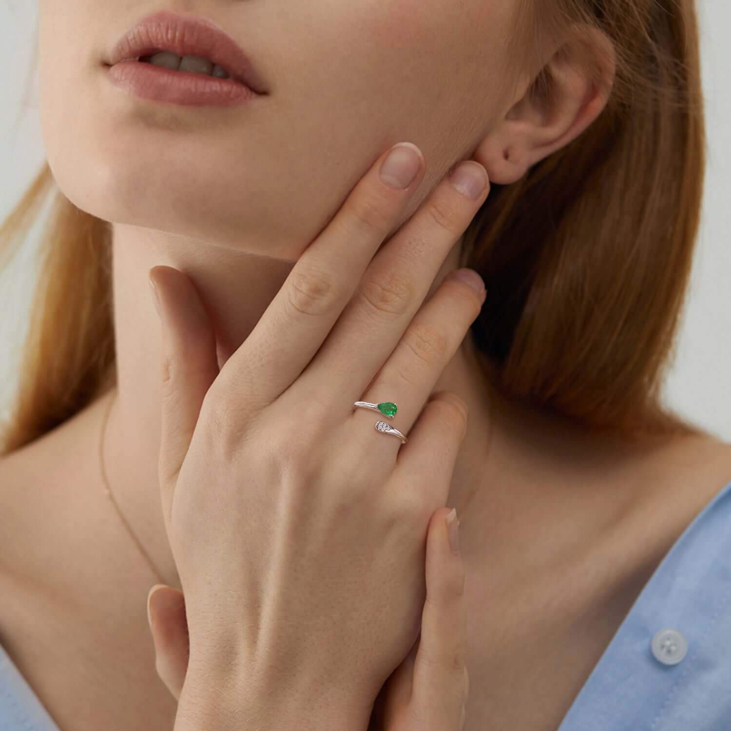 Close-up of a woman wearing an emerald ring on her finger, with a blurred background.