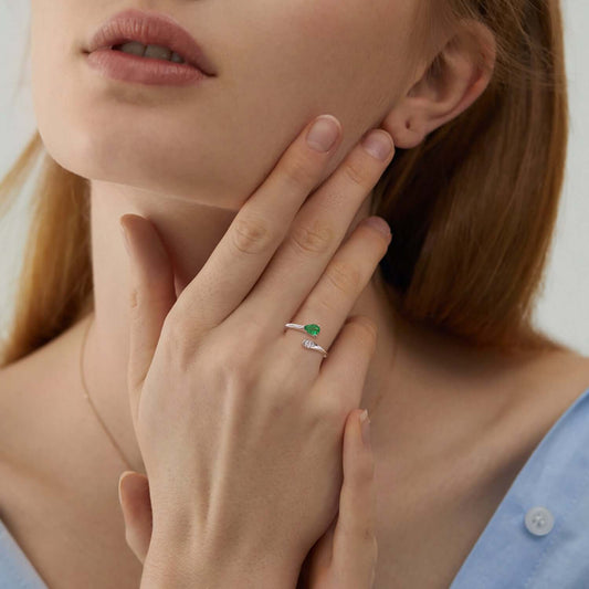 Close-up of a woman wearing an emerald ring on her finger, with a blurred background.