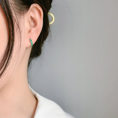 Close-up of an ear wearing a green hoop earring with a neutral background