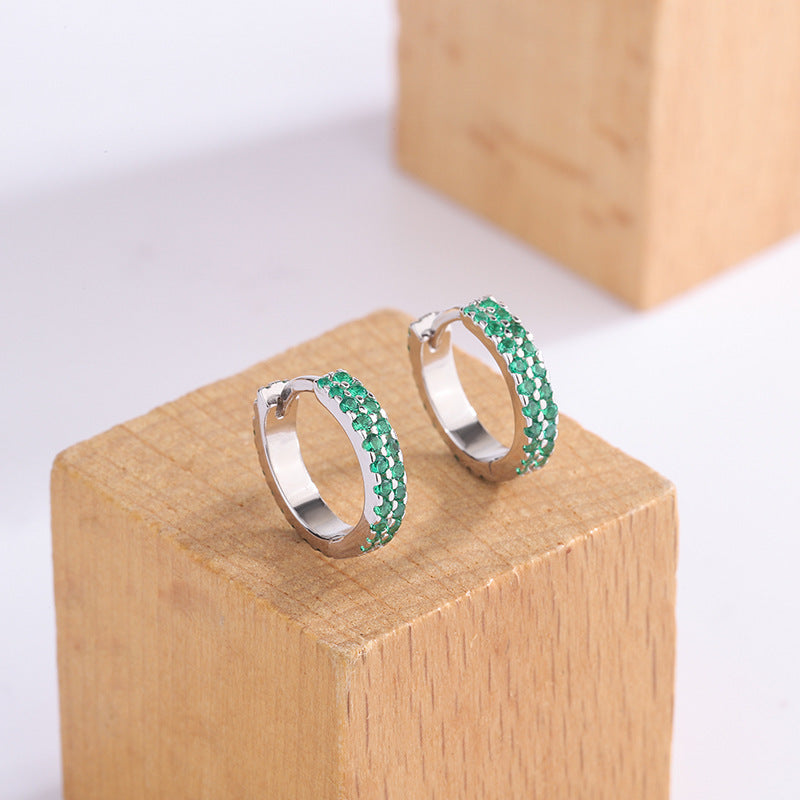 Pair of silver hoop earrings with green gemstones on a wooden block.