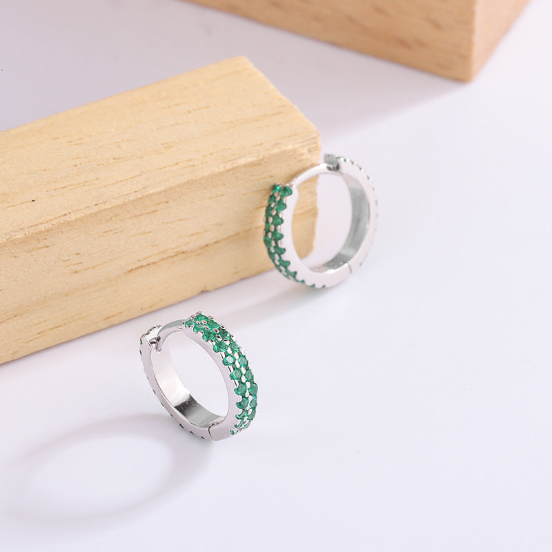 Silver hoop earrings with green gemstones on a light background