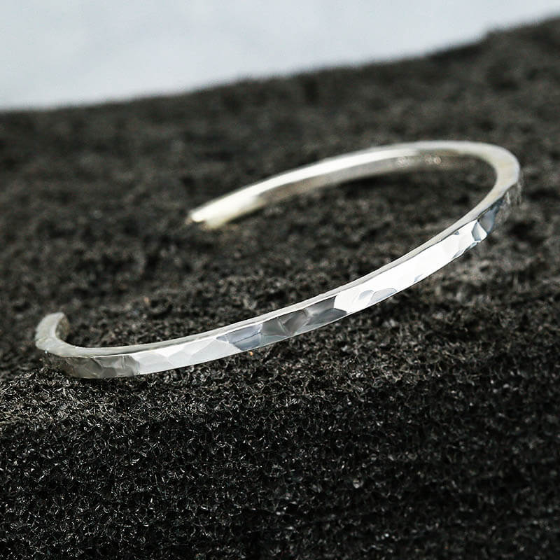 Silver hammer bracelet on a textured black surface.