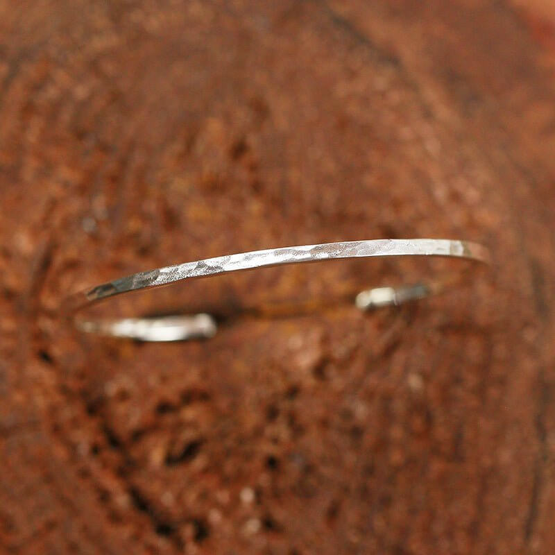 Silver hammer bracelet on a textured brown surface.