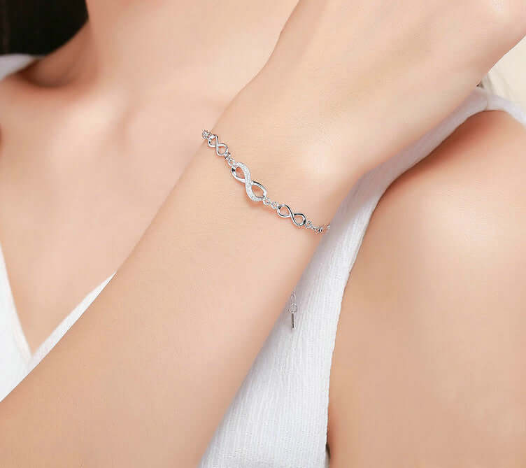Silver bracelet with three infinities designs on a person's wrist with a blurred background