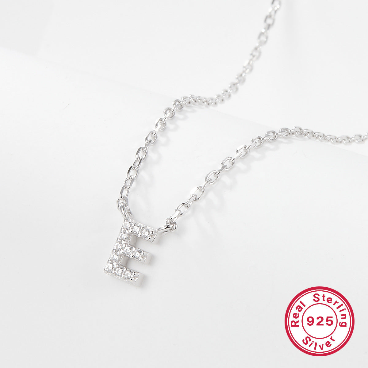 Silver necklace with a letter 'E' pendant on a white background, featuring a 'Real Sterling Silver 925' stamp.