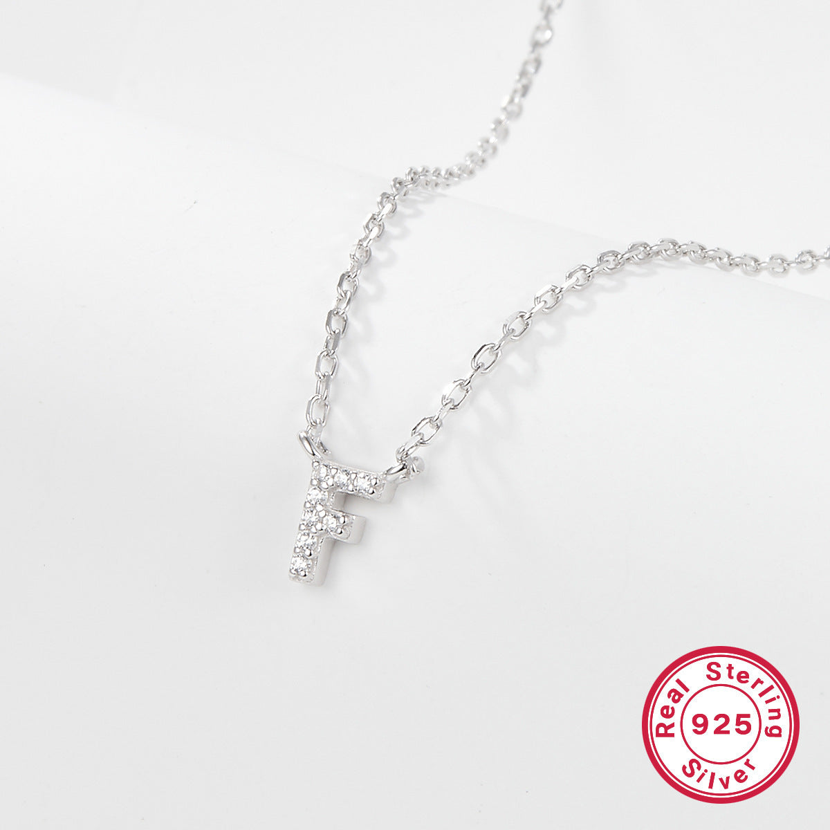 Silver necklace with a letter 'F' pendant on a white background, featuring a 'Real Sterling Silver 925' stamp.