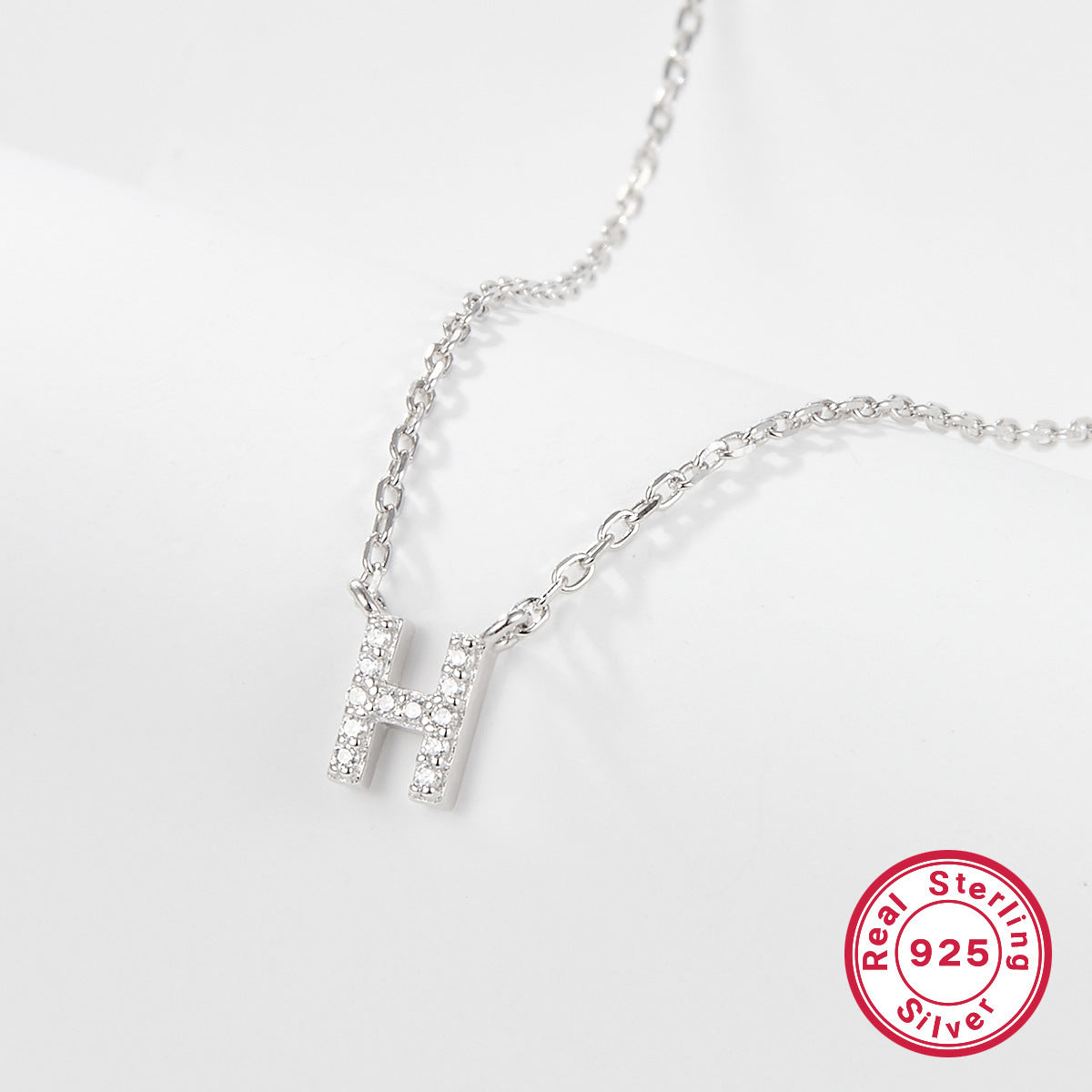 Silver necklace with a letter 'H' pendant on a white background, featuring a 'Real Sterling Silver 925' stamp.
