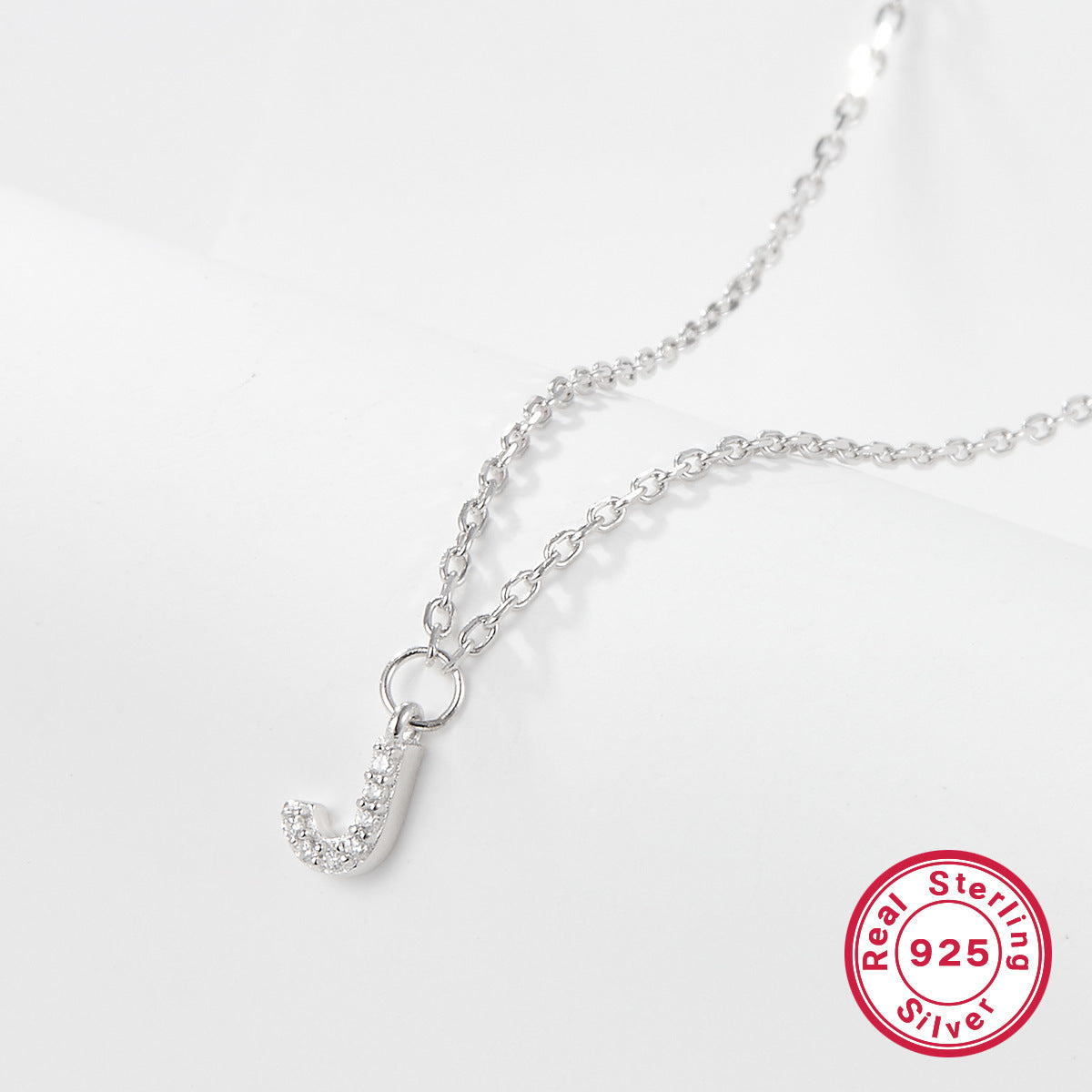 Silver necklace with a letter 'J' pendant on a white background, featuring a 'Real Sterling Silver 925' stamp.