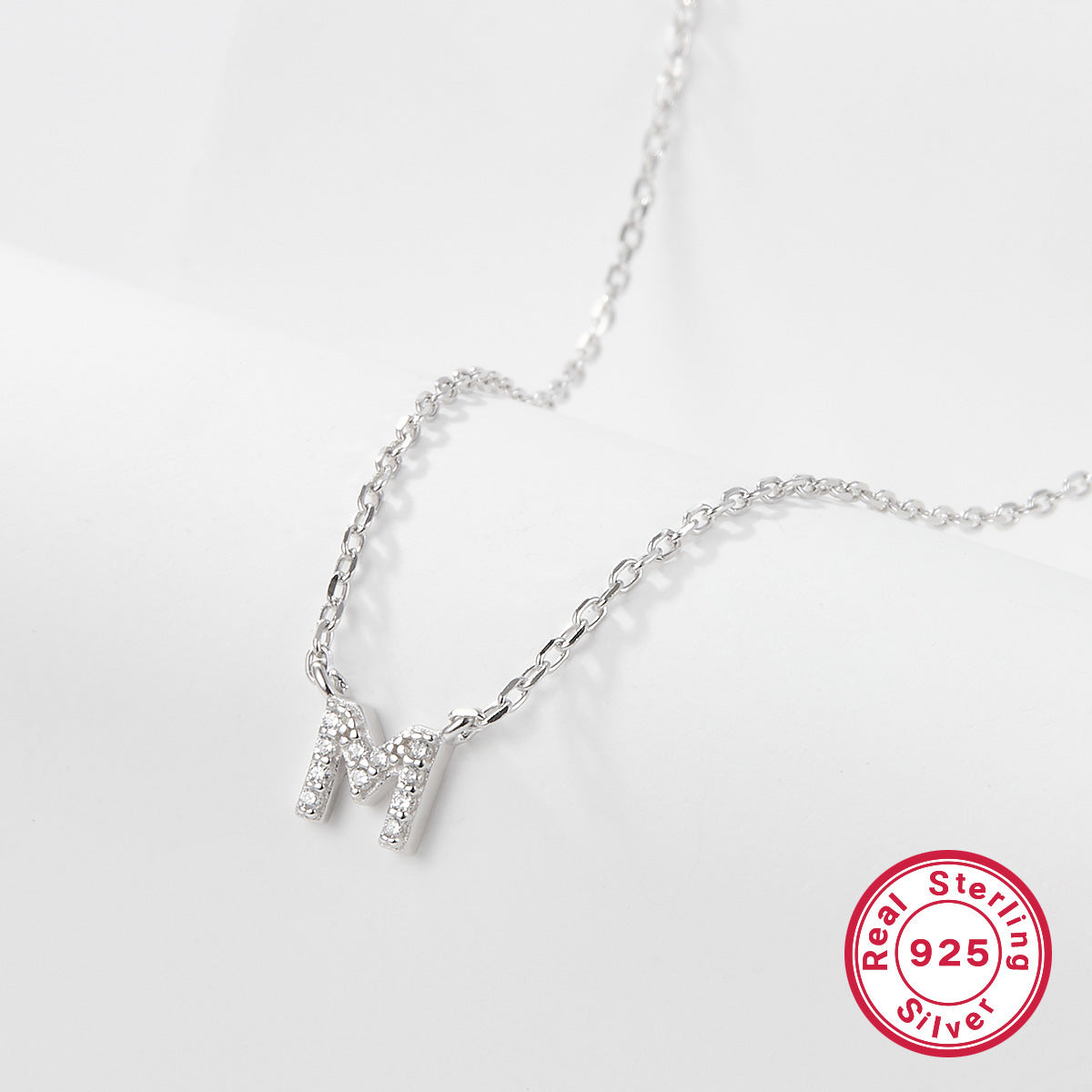 Silver necklace with a letter 'M' pendant on a white background, featuring a 'Real Sterling Silver 925' stamp.