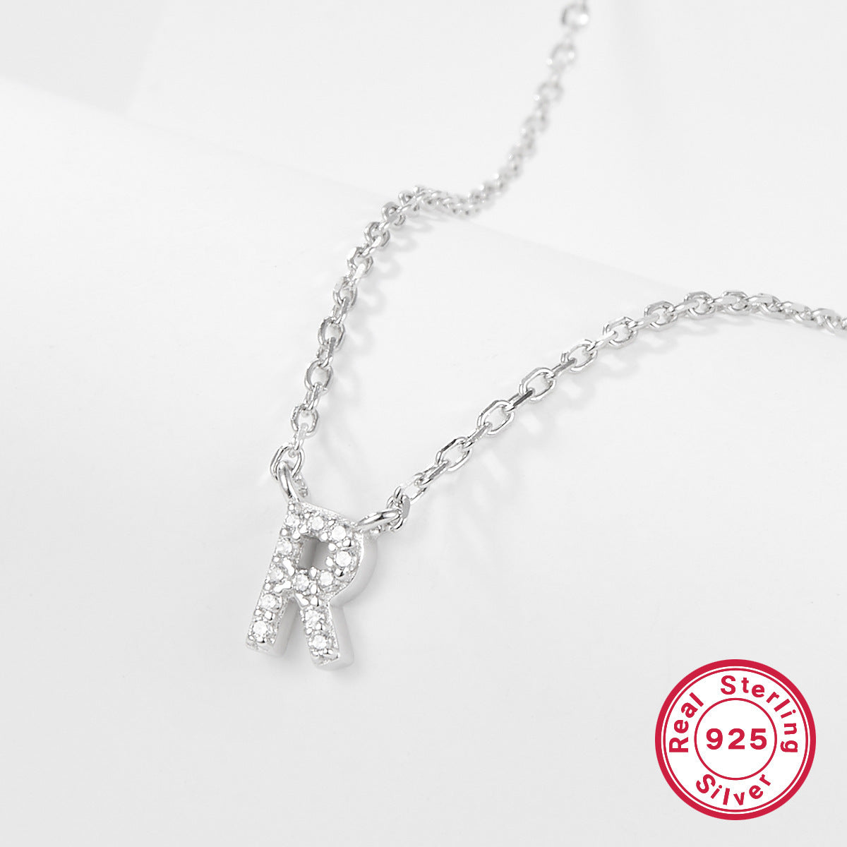 Silver necklace with a letter 'R' pendant on a white background, featuring a 'Real Sterling Silver 925' stamp.