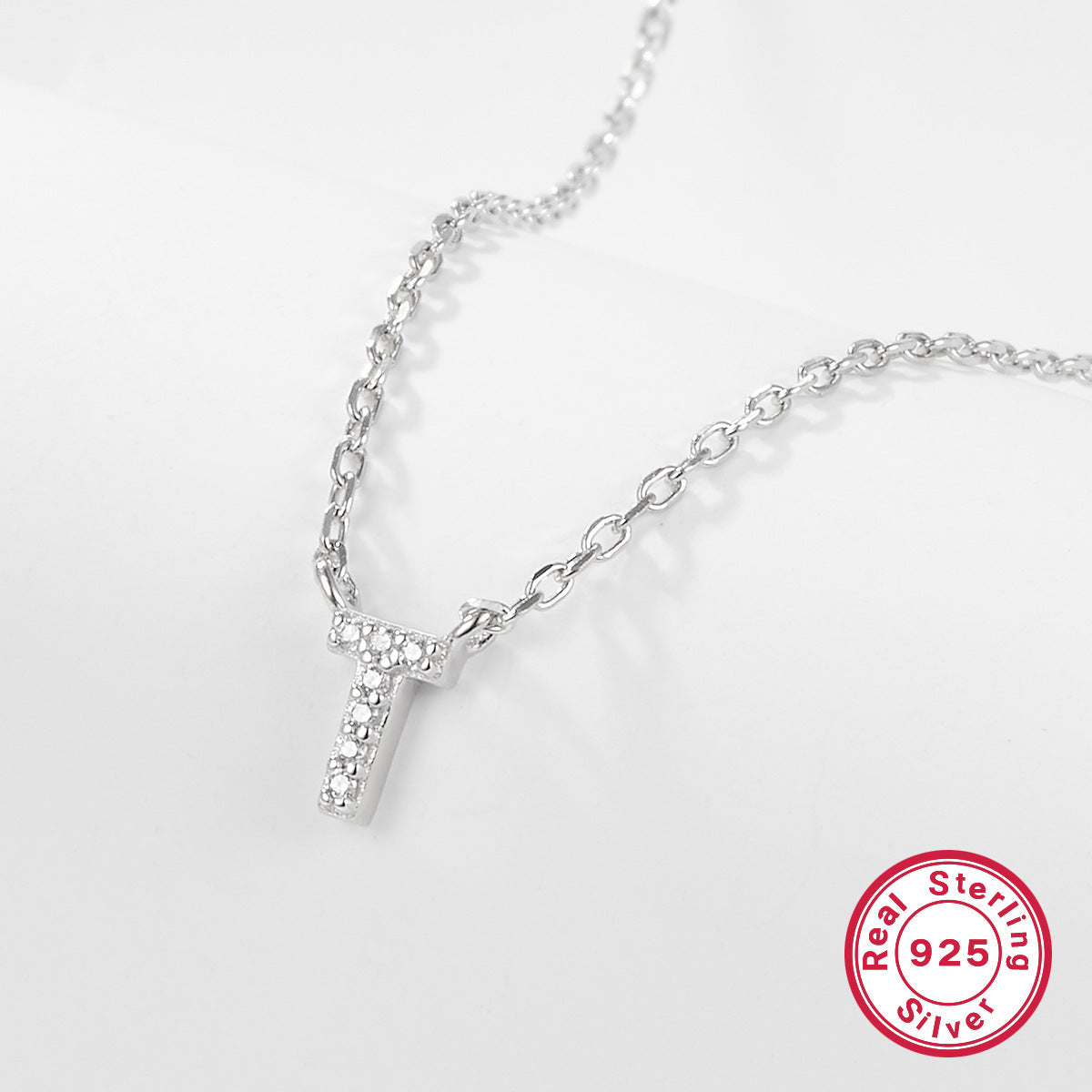 Silver necklace with a letter 'T' pendant on a white background, featuring a 'Real Sterling Silver 925' stamp.