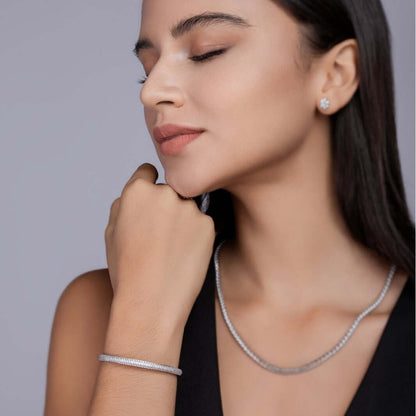 Woman wearing a silver necklace,  moissanite bracelet, and earrings against a gray background