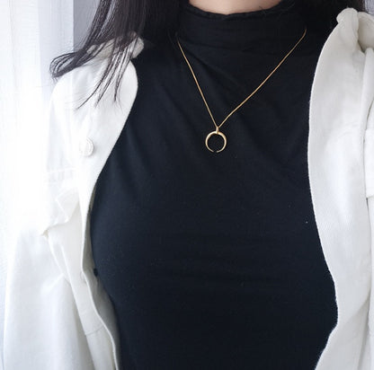 Person wearing a black top and white jacket with a gold necklace featuring a moon pendant.