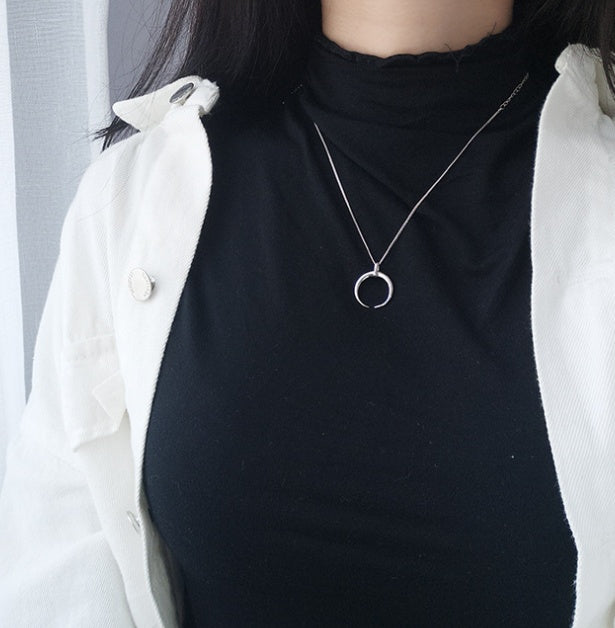 Person wearing a black top with a silver necklace featuring a moon pendant.