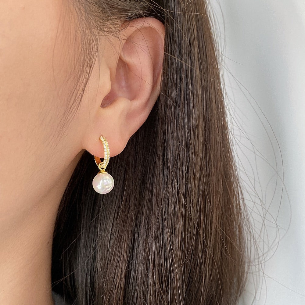 Gold earring with a pearl on an ear against a neutral background