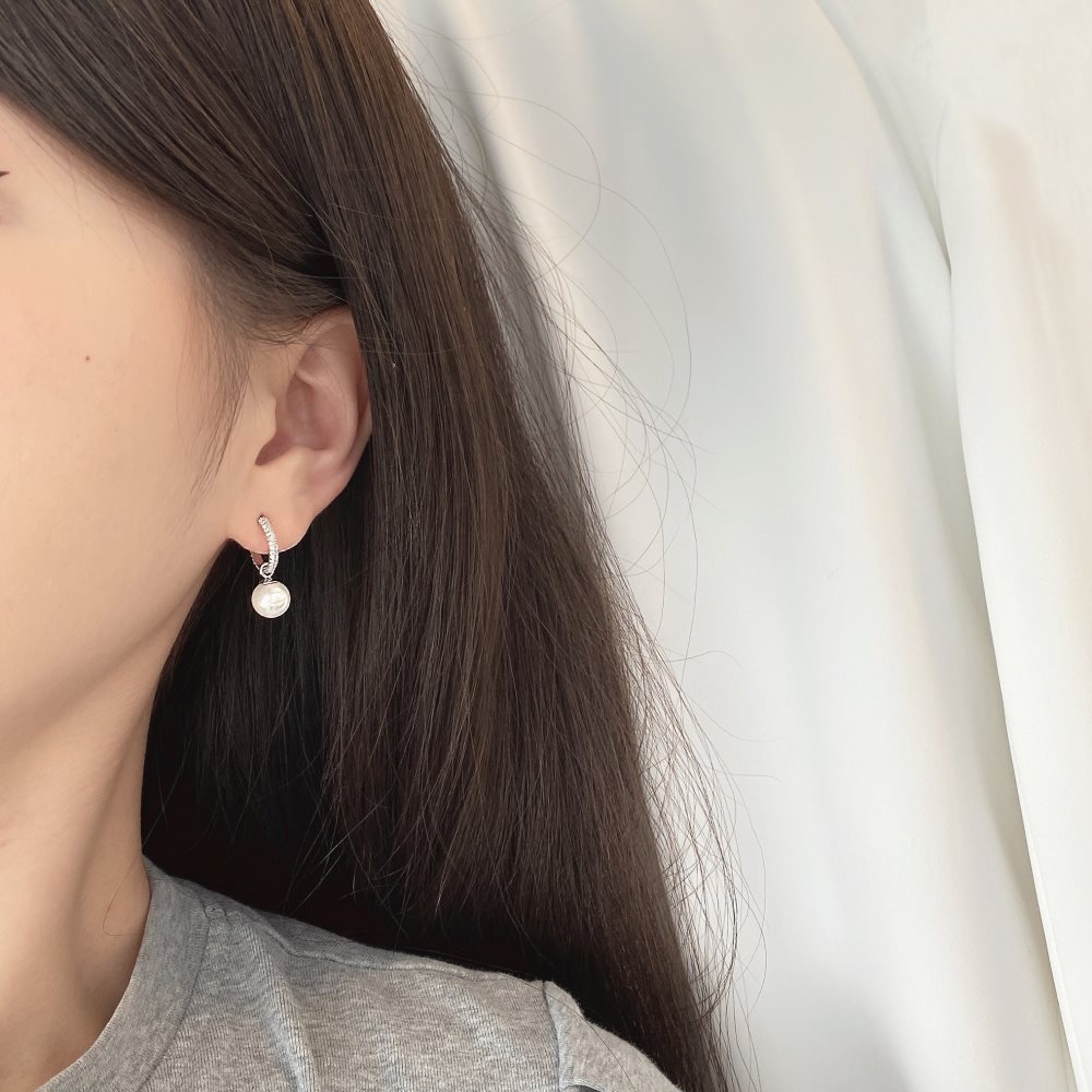 Close-up of a person wearing silver pearl earrings with a neutral background