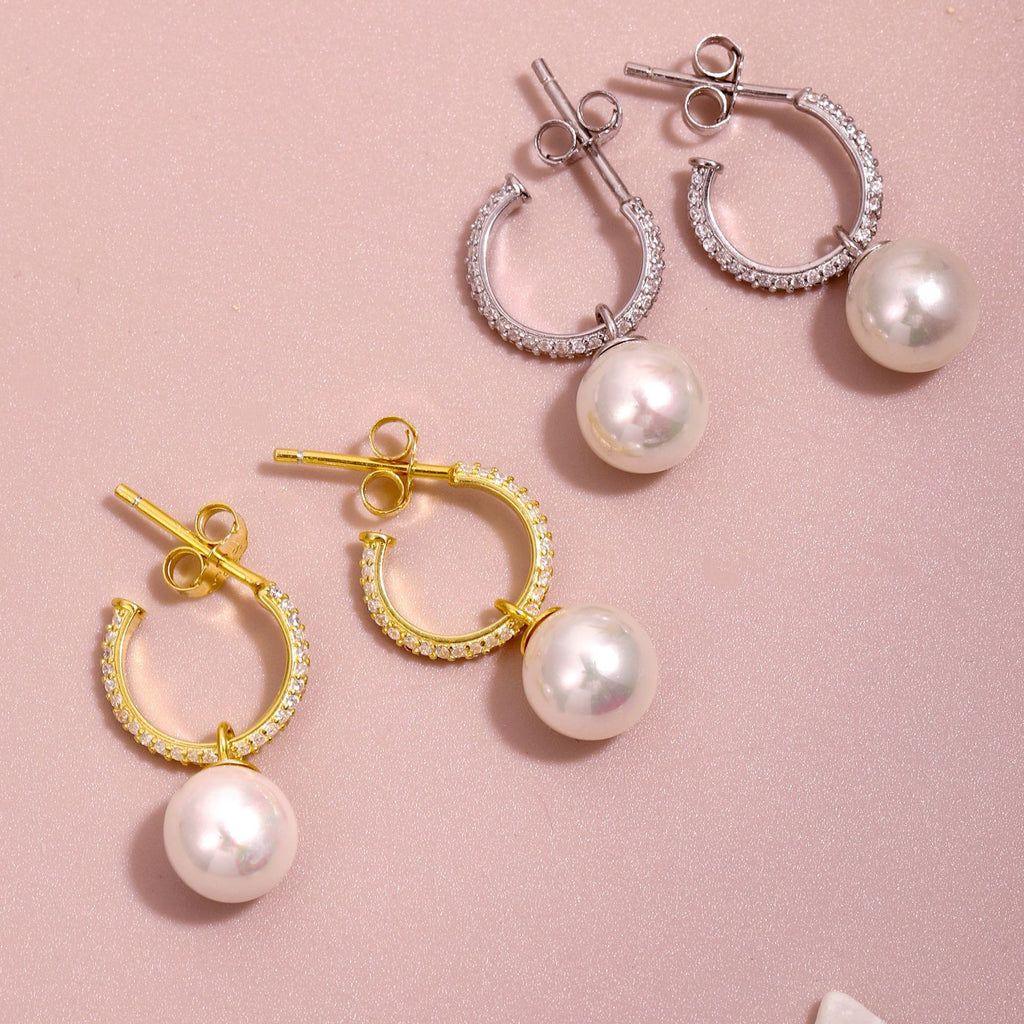 Pair of silver and gold hoop earrings with pearl drops on a pink background