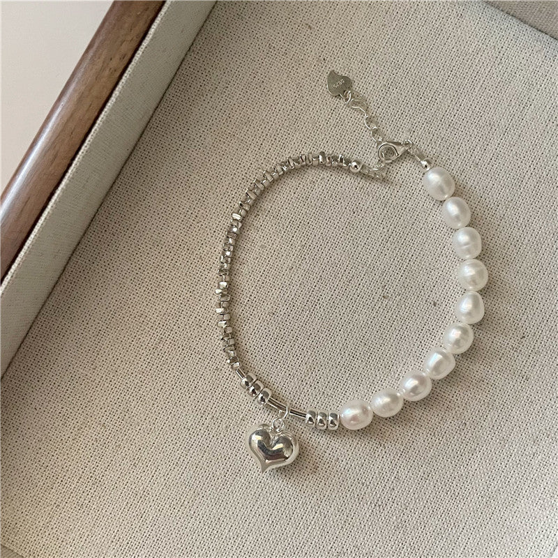 Pearl bracelet with silver beads and heart charm on a neutral background
