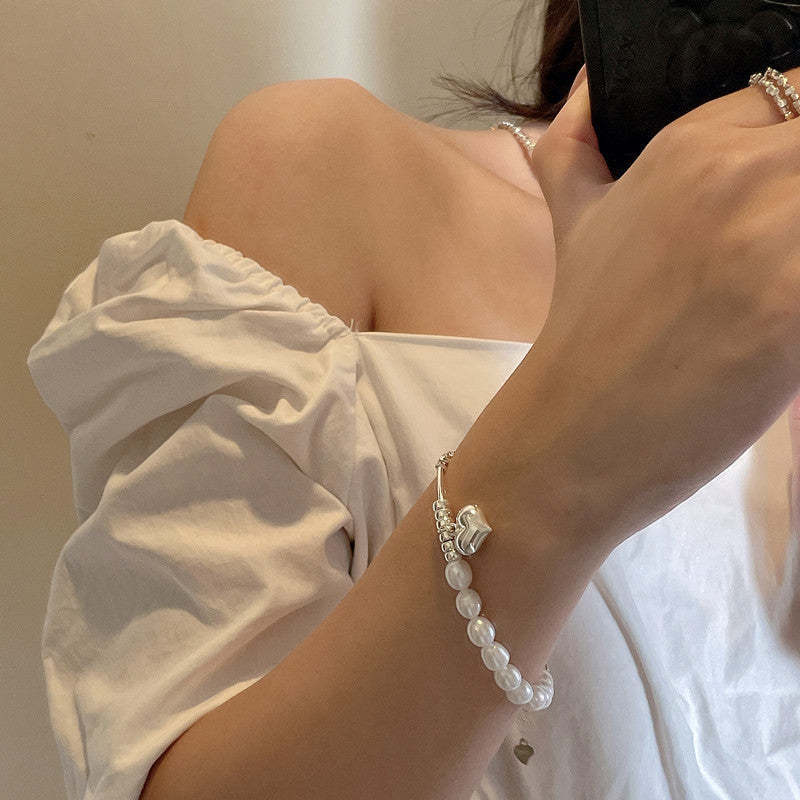 Person wearing a pearl bracelet with silver beads and heart charm with a neutral background