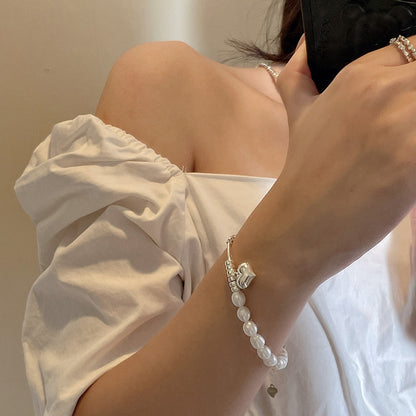 Person wearing a pearl bracelet with silver beads and heart charm with a neutral background