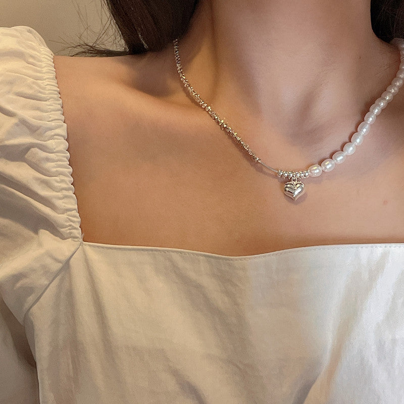 Pearl necklace with a heart-shaped charm worn by a person in a white top.