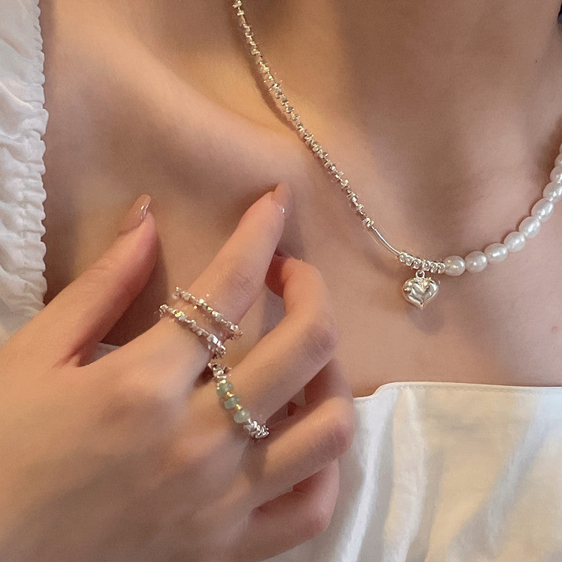 Pearl necklace with heart charm and silver beads worn by a person, close-up of hand and necklace.