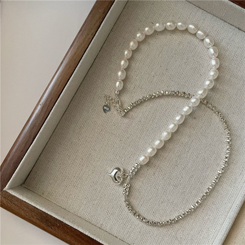 Pearl necklace with silver beads and heart charm on a textured surface